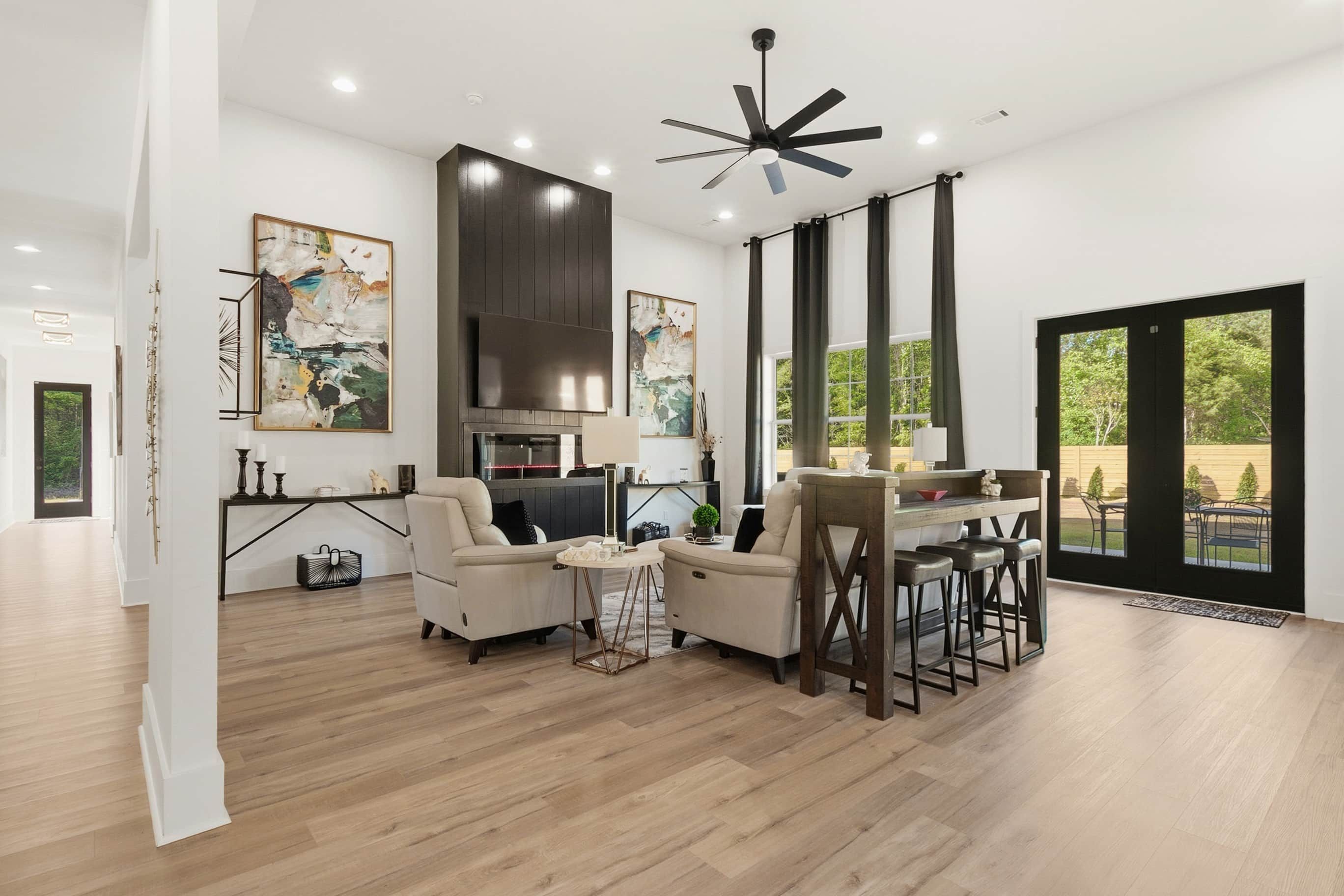 A modern living room with a fireplace, a dining area with bar stools, and large windows offering a view of the outdoors.