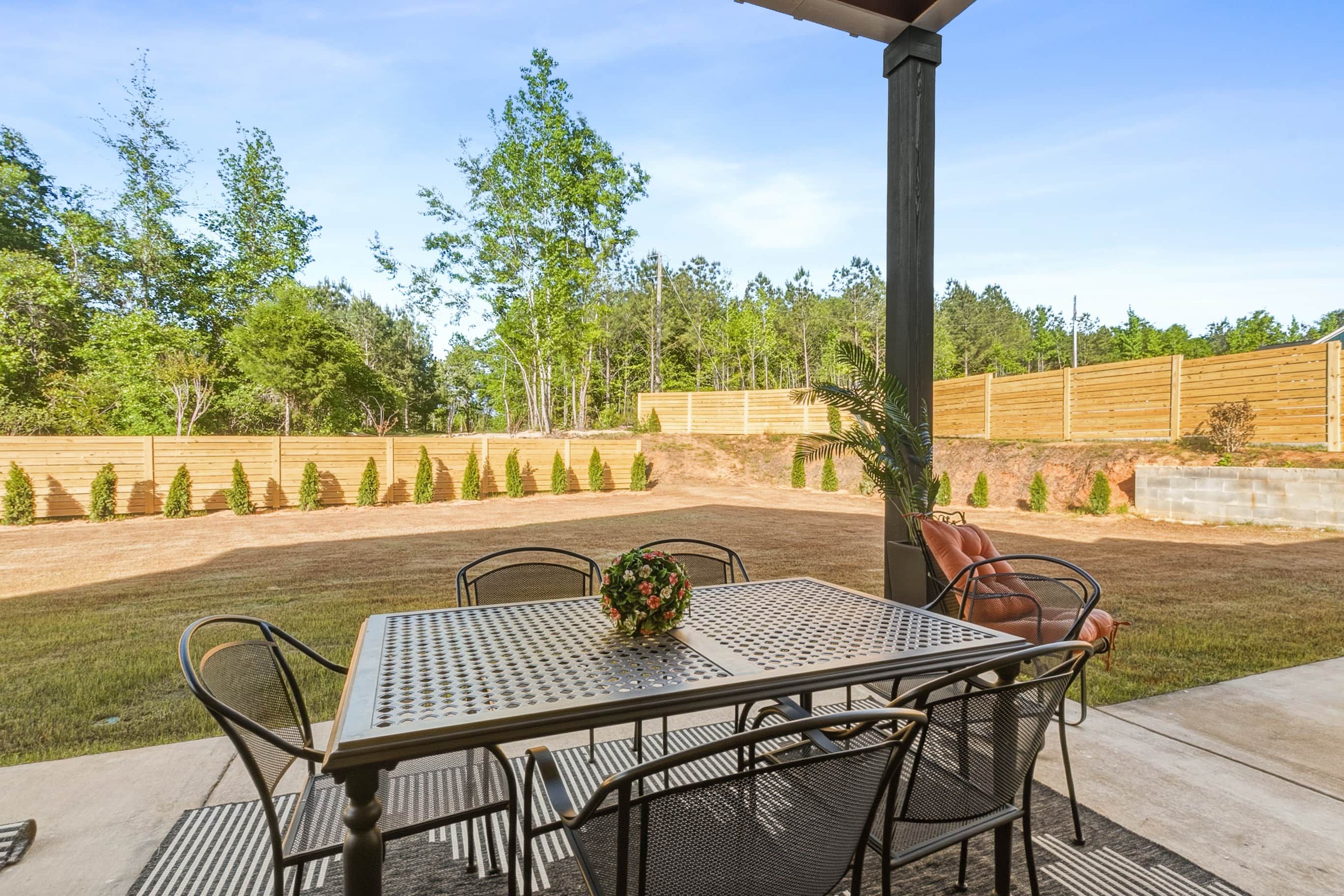 An outdoor patio with a table and chairs, surrounded by a wooden fence and trees.