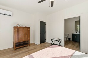A bedroom with a wooden wardrobe, a bed with a pink blanket, a ceiling fan, and a door leading to a bathroom. - The Retreat - South of the River (Fosters)
