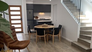 A modern kitchen with dark cabinets, a central island, and a dining area with a round table and chairs.
