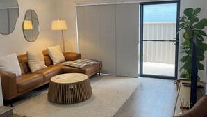 A modern living room with a brown leather sofa, a round wooden coffee table, and a large potted plant.