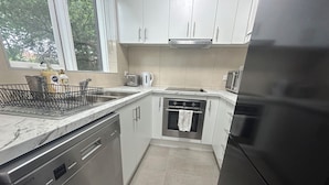 A compact kitchen with white cabinets, a stainless steel dishwasher, a built-in oven, and a refrigerator. - Need a dose of Vitamin Sea? (Elwood)