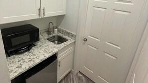 A compact kitchen with white cabinets, a microwave, a sink, and a dishwasher.