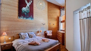 Un dormitorio con paneles de madera, una cama, mesitas de noche, una silla y un aparador.