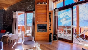 Una habitación acogedora con chimenea, paredes de madera y ventanas amplias con vistas a la montaña.