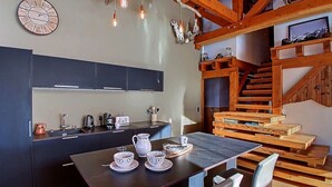 Una cocina moderna con armarios oscuros, una mesa de comedor dispuesta con tazas y un hervidor, y una escalera de madera que conduce a una zona en loft.