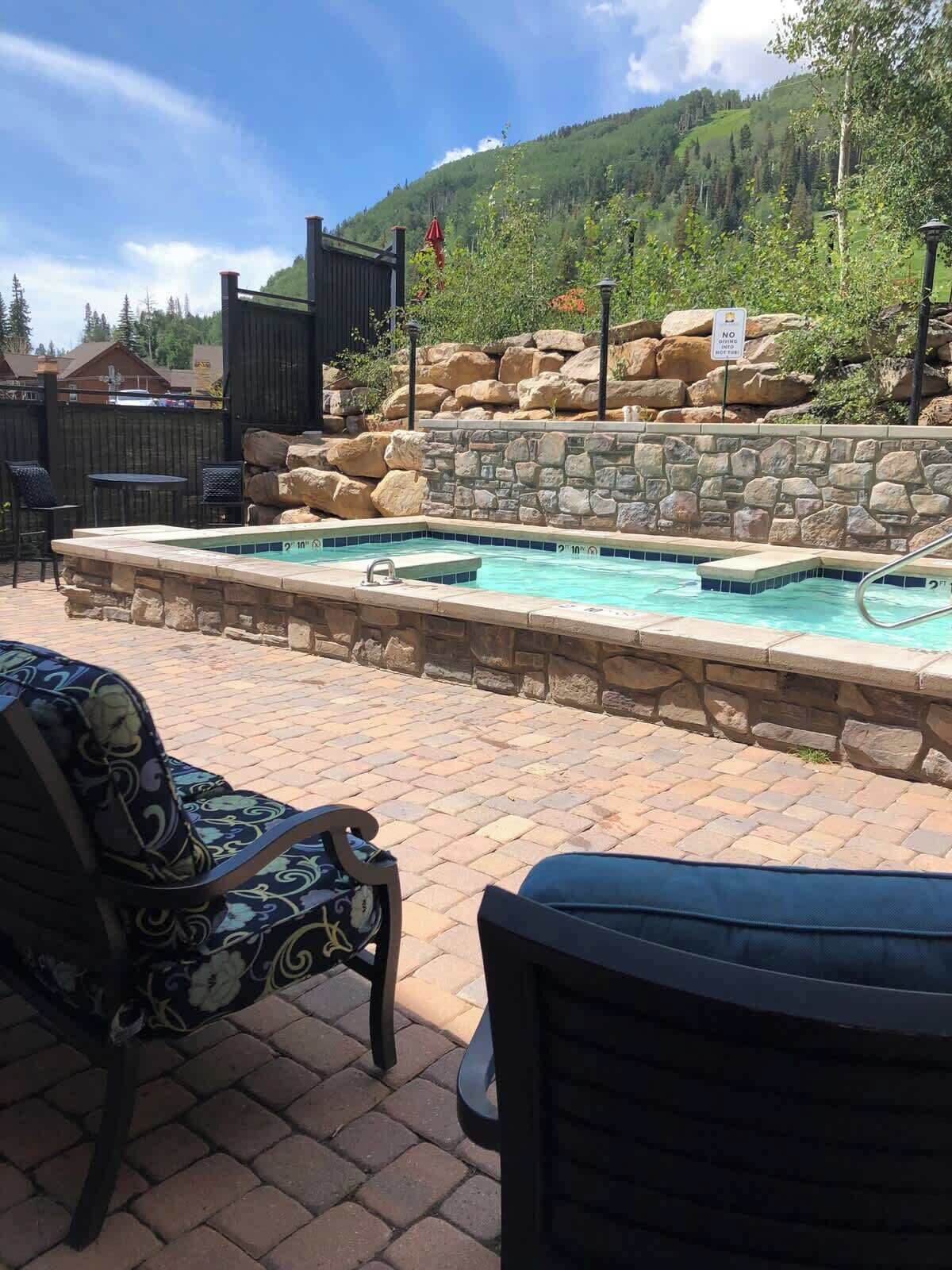 A pool with stone walls, two chairs, and a view of a mountain.