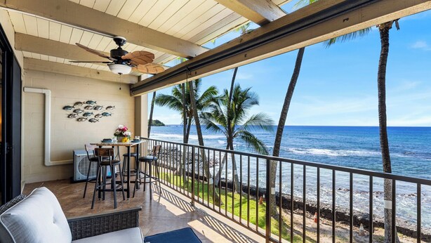 Un balcon avec vue sur l’océan, un ventilateur de plafond et une table avec des chaises.