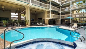 Une piscine avec un jacuzzi, entourée de chaises longues et un bâtiment à plusieurs niveaux doté de balcons.