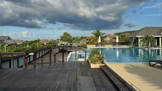 Eine Holzterrasse mit Pool und Liegestühlen, mit Blick auf eine Wohngegend mit Häusern und blauem Himmel.