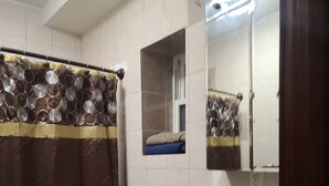 Kylpyhuone, jossa on suihkuverho, wc, pesuallas, jossa on saippua-annostelija, ja peili.