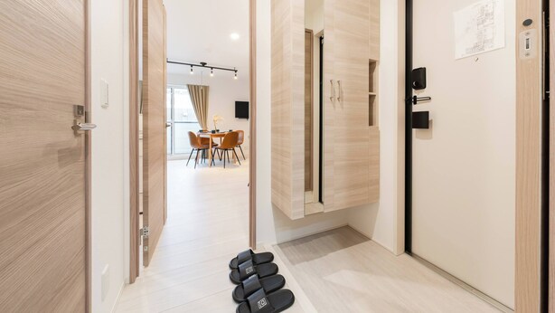 Une chambre d’hôtel moderne avec une porte en bois, un miroir, une armoire et une paire de chaussons posés sur le sol.