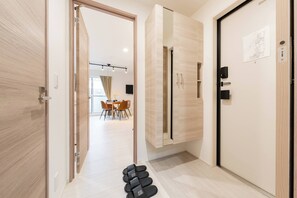 A modern hotel room with a wooden door, a mirror, a wardrobe, and a pair of slippers on the floor. - House Hotel Ekoda (Tokyo)