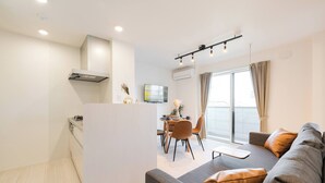 Un salon moderne comprenant un canapé, un coin repas avec des chaises, un téléviseur et un coin cuisine avec une cuisinière.
