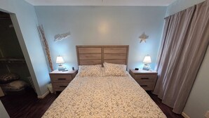 Un lit bien fait, avec une literie à motifs, deux tables de chevet avec des lampes, une étoile de mer décorative accrochée au mur et un rideau à la fenêtre.