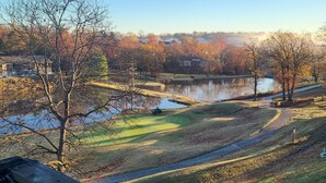 Une vue depuis un balcon donnant sur un terrain de golf, avec un lac, des arbres et un pont.