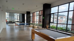 A spacious room with a pool table, comfortable seating, and large windows offering a city view.