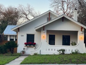 A single-story house with a white exterior, number 139, featuring a front porch with two windows and a small entryway. - A guest favorite! Charming 2-bedroom house- stylish comfort in a great area (San Antonio)
