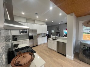 A modern kitchen with white cabinets, stainless steel appliances, and a wooden ceiling. - A guest favorite! Charming 2-bedroom house- stylish comfort in a great area (San Antonio)