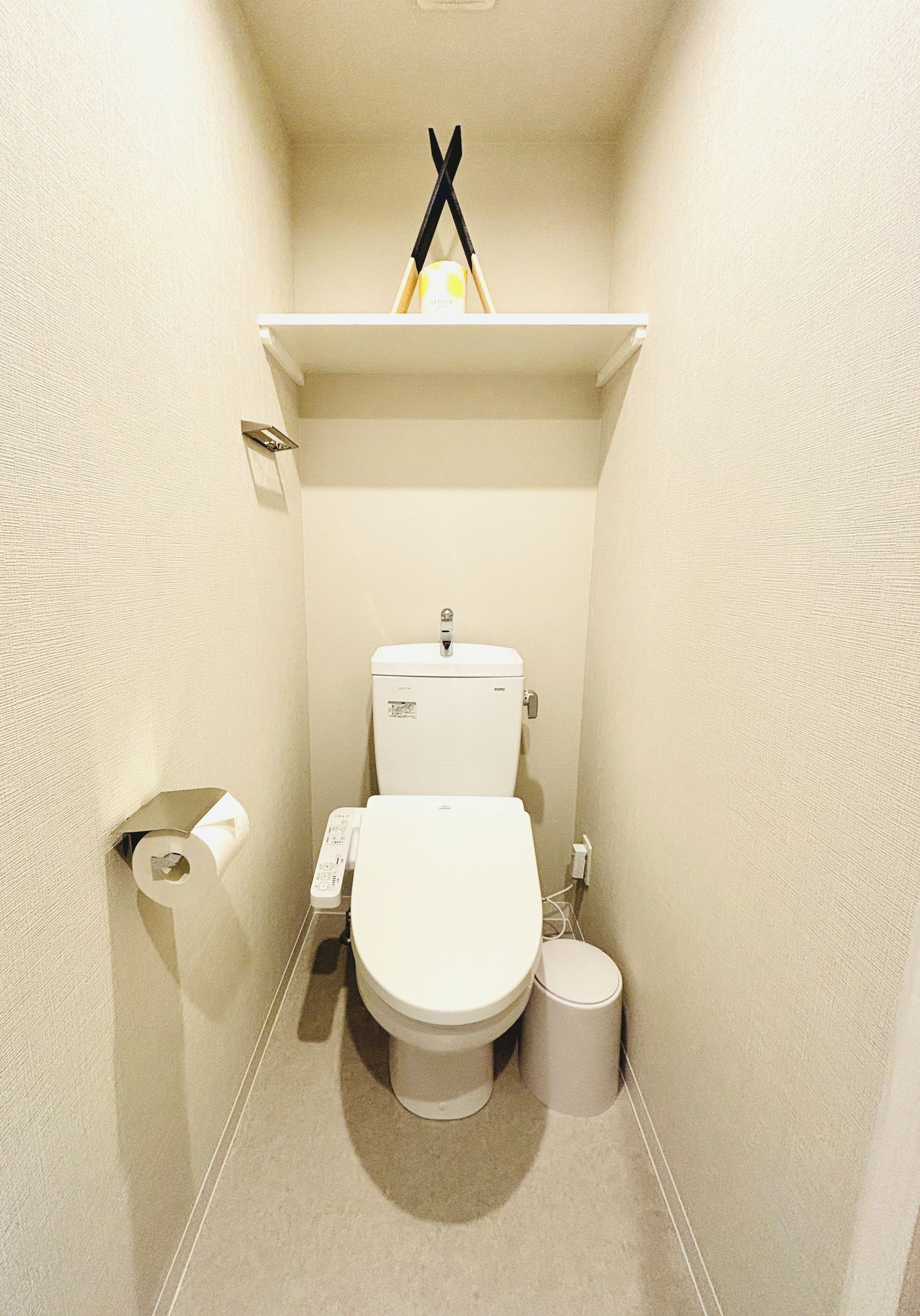 A small, compact bathroom with a toilet, a toilet paper holder, and a trash bin.