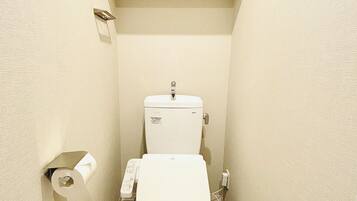 A small, compact bathroom with a toilet, a toilet paper holder, and a trash bin.