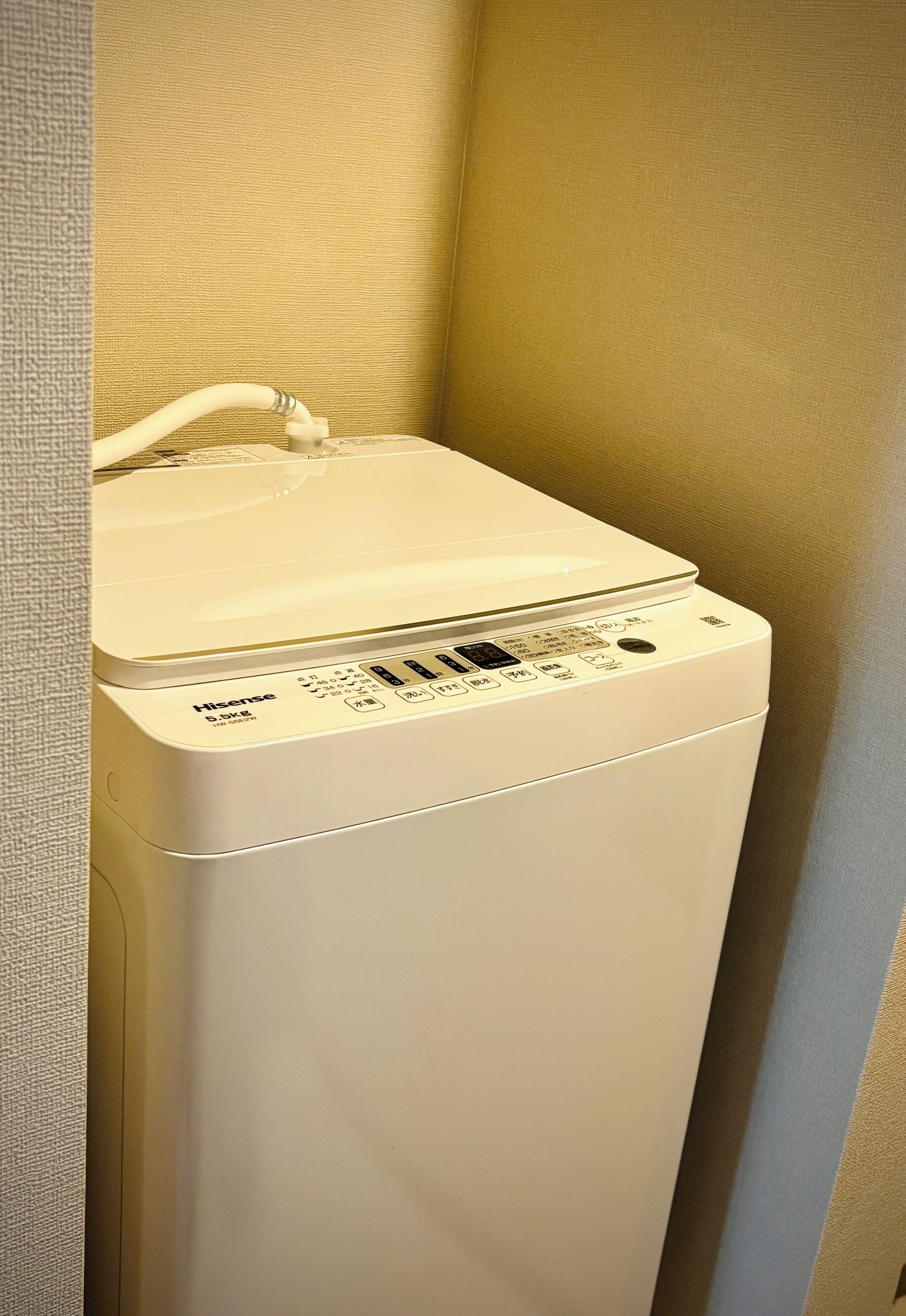 A white Hisense washing machine in a corner of a room with beige walls.
