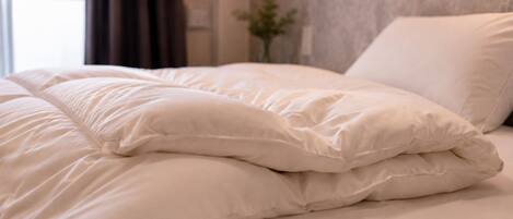 A neatly made bed with white bedding and pillows, a wall-mounted light fixture, and a window with curtains.