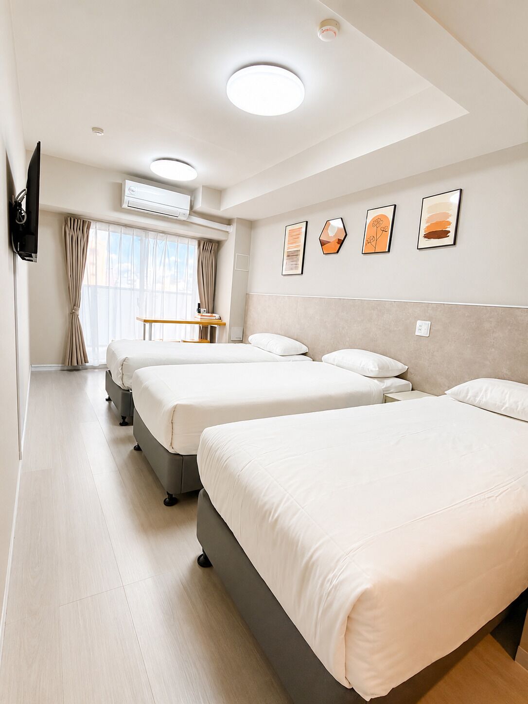 Ein Hotelzimmer mit drei Betten, einem Fernseher, einer Klimaanlage und einem Fenster mit Vorhängen.