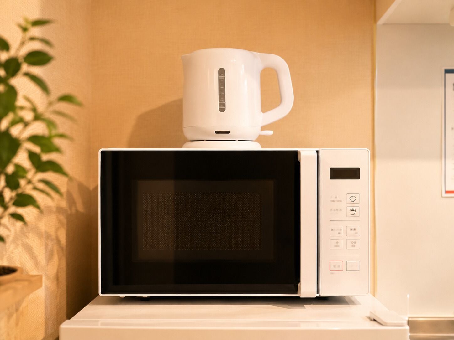 Un microondas blanco con una cafetera encima, sobre una encimera blanca.