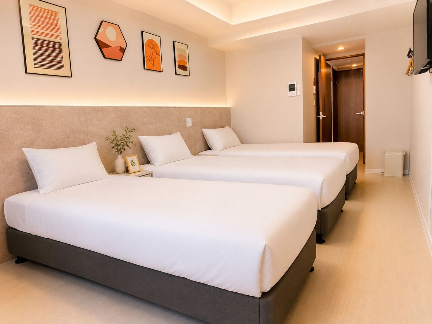A hotel room with two beds, a nightstand, a vase with a plant, and artwork on the wall.