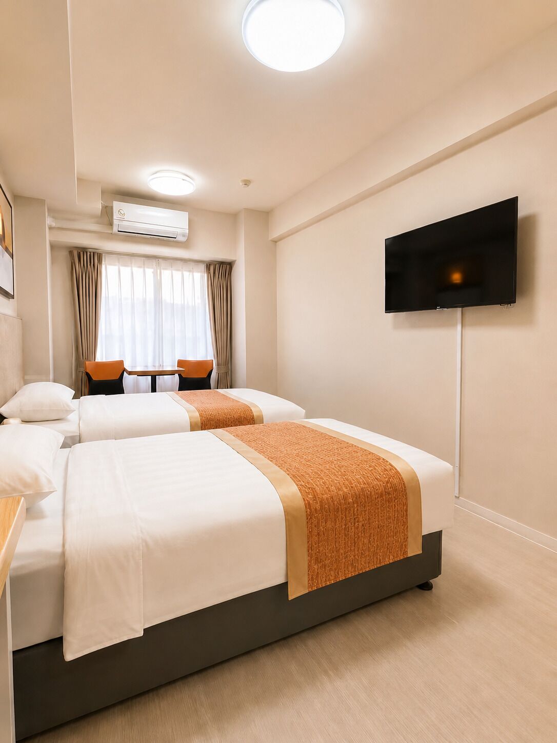 Een hotelkamer met twee bedden, een televisie, een tafel met stoelen en een airconditioning.