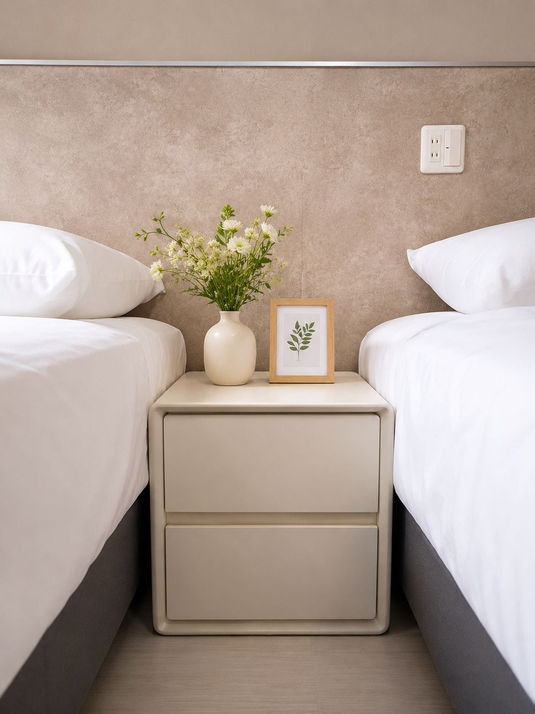 A bedroom with two beds, a bedside table with a vase of flowers, and a framed picture.