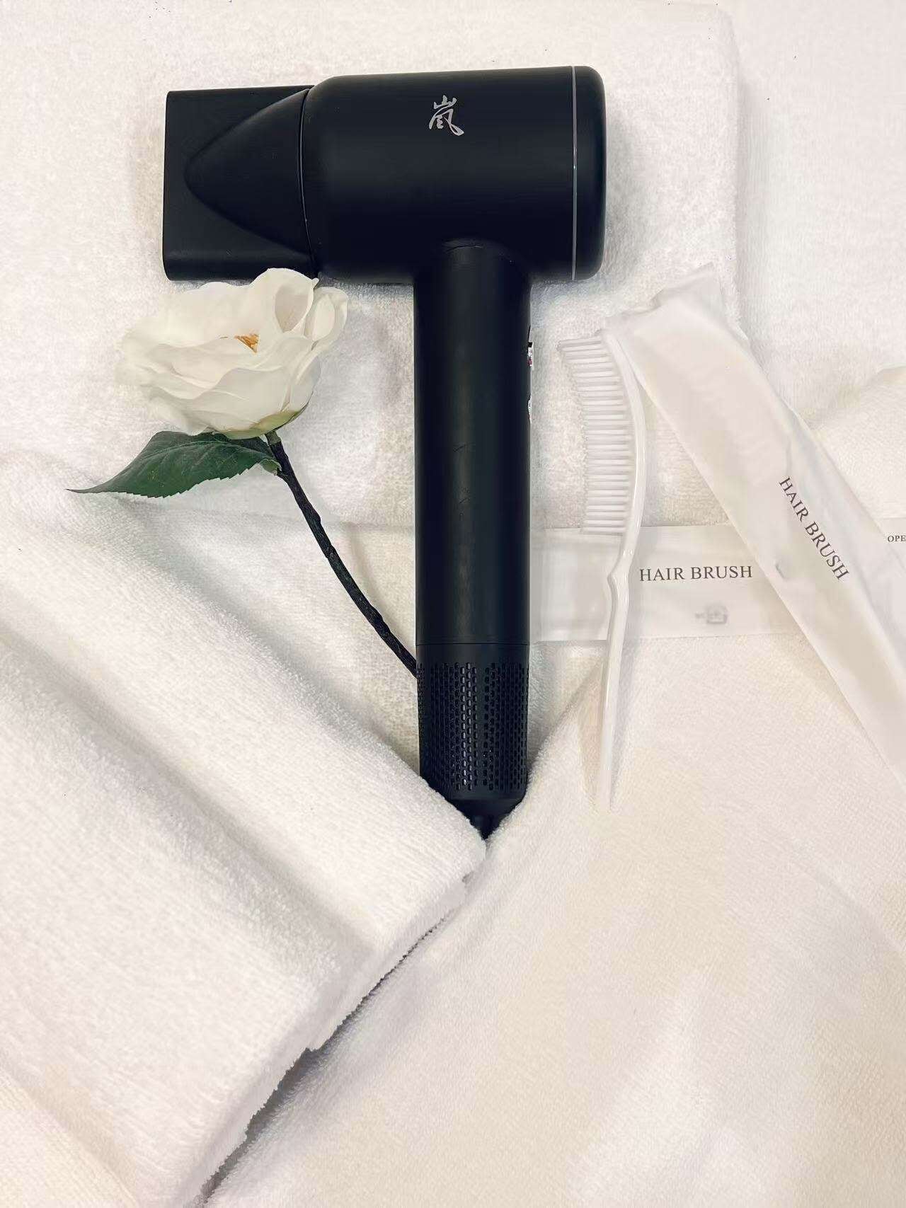 Un secador de pelo negro con cable, sobre una toalla blanca con una rosa blanca.