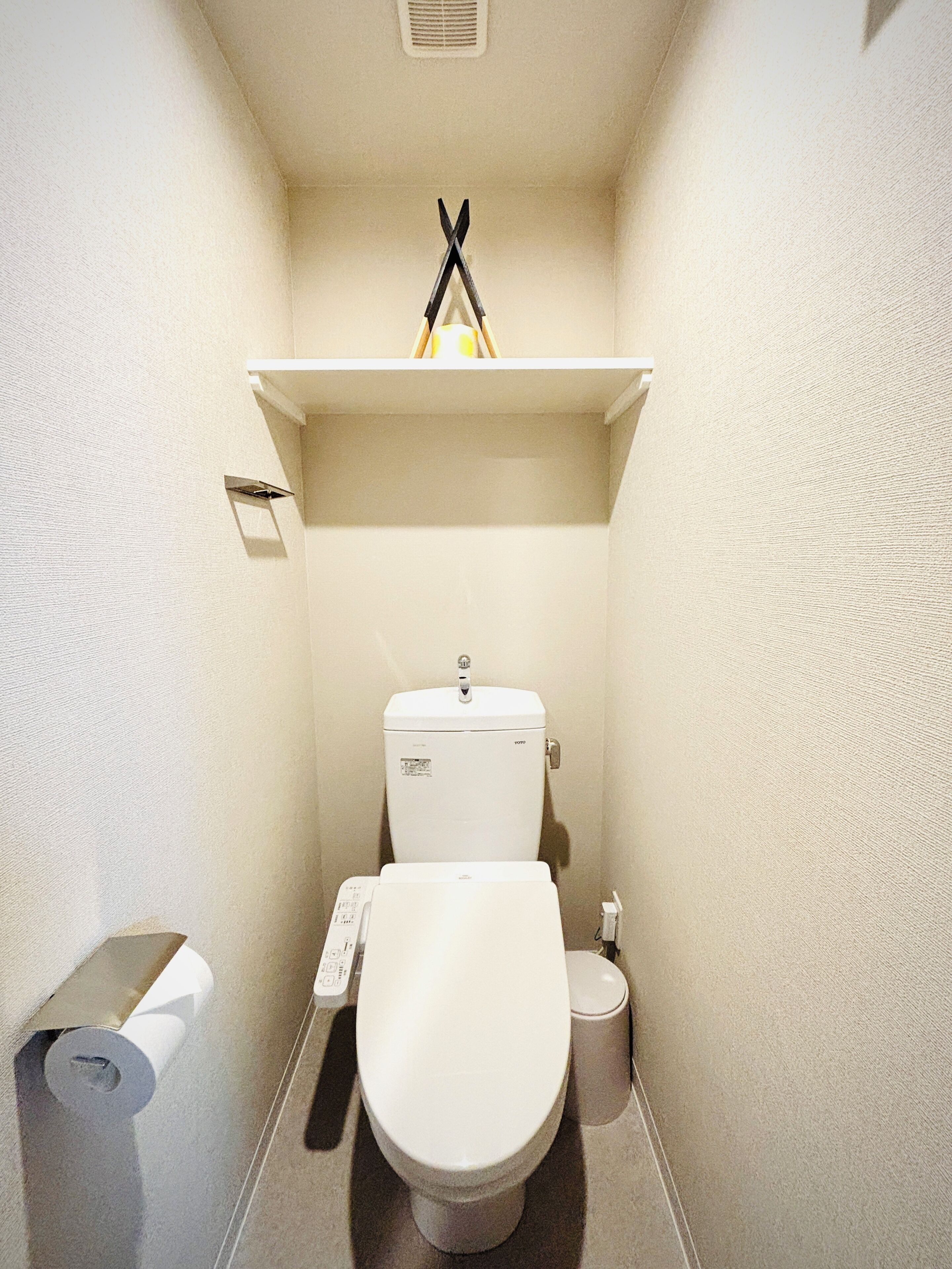 Ein kleines, kompaktes Badezimmer mit Toilette, Toilettenpapierhalter und Ablage über der Toilette.