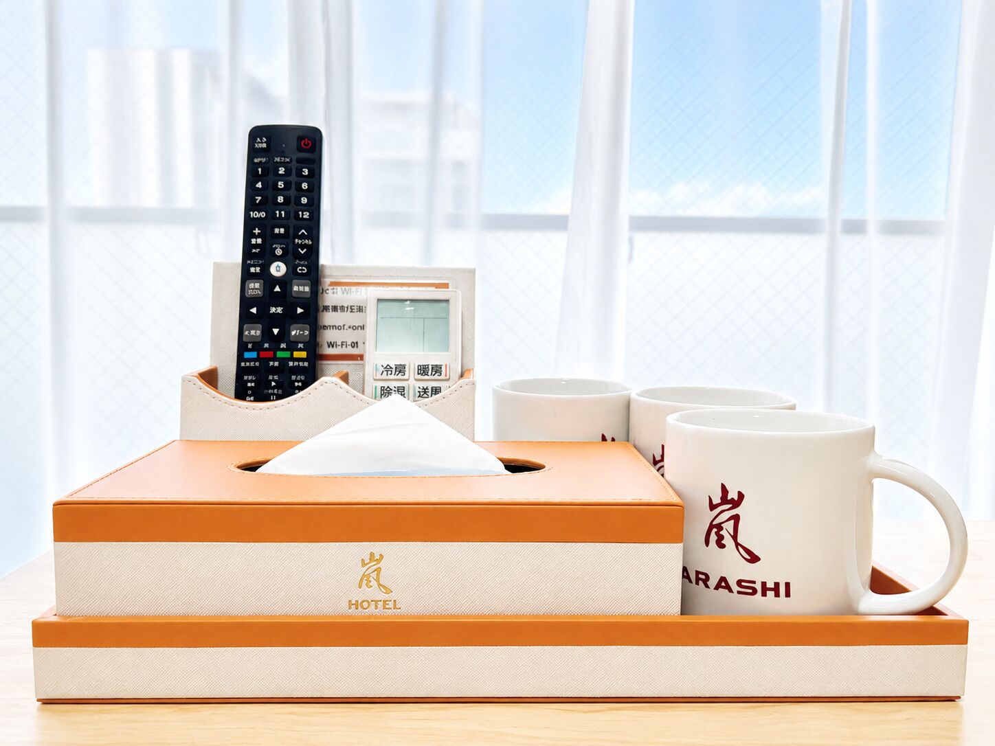 A hotel room with a remote control, a card, and a mug on a tray.