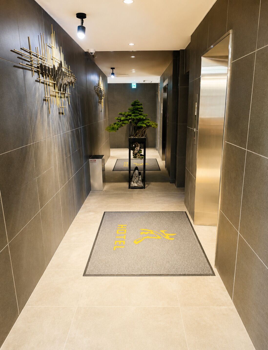A modern hotel corridor with a reception desk, a potted plant, and a 'HOTEL' sign on the floor.