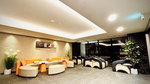 Un espace de détente moderne, avec des canapés et des fauteuils, un sol carrelé et un mur décoratif.