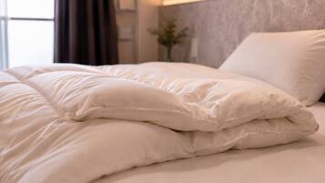 A neatly made bed with white bedding and pillows, a wall-mounted light fixture, and a window with curtains.