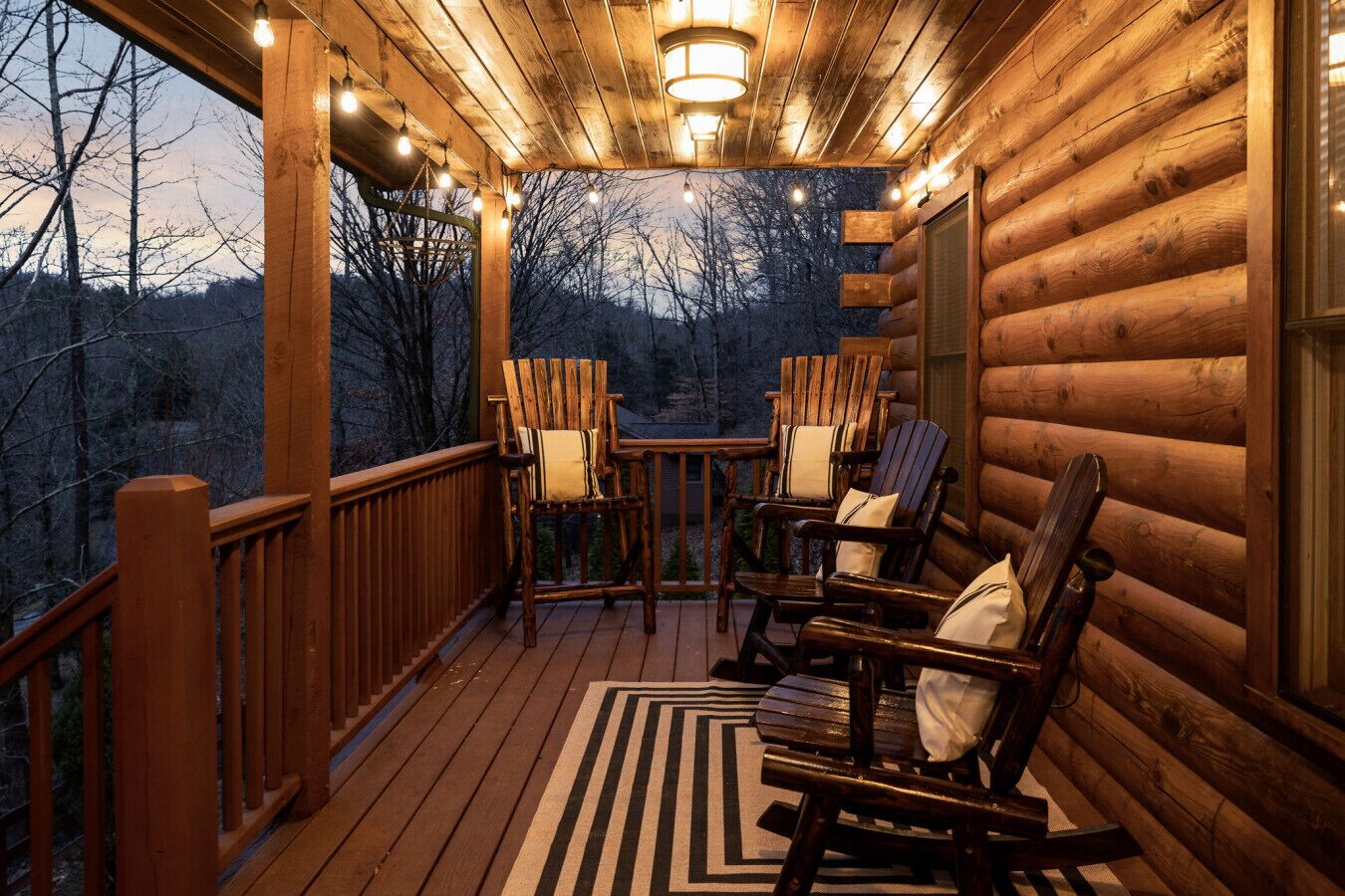 Una terraza de madera con mecedoras y una mesa, con vista a una zona boscosa.
