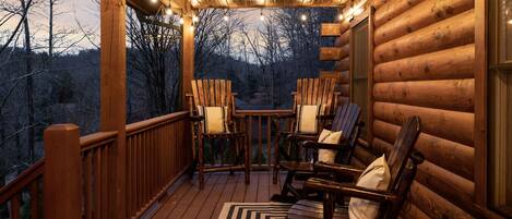Una terraza de madera con mecedoras y una mesa, con vista a una zona boscosa.