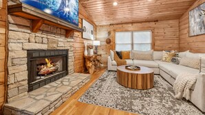 A cozy living room with a stone fireplace, a large flat-screen TV, a wooden ceiling, and a comfortable sofa set.