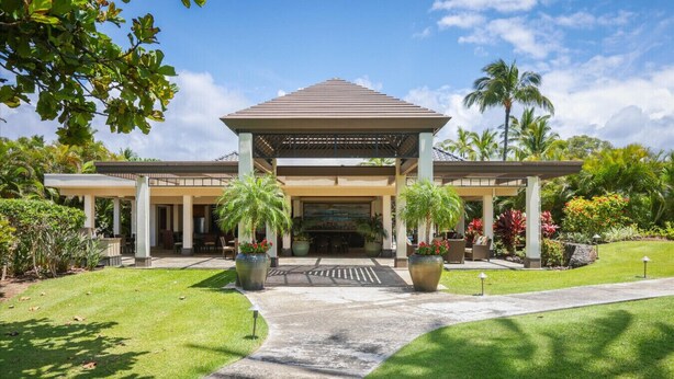 A hotel entrance with a covered walkway, palm trees, and a well-maintained lawn.
