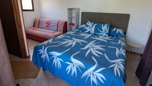 Een slaapkamer met een groot bed, een kleine bank, een houten nachtkastje en een hanglamp.