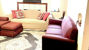 Un salon avec un canapé beige, un fauteuil rouge et un tapis à motifs.