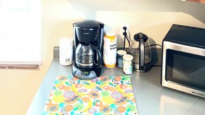 Une cuisine avec un meuble en bois contenant divers ustensiles de cuisine et des produits alimentaires, une machine à café, un mixeur et un four à micro-ondes posés sur le plan de travail.