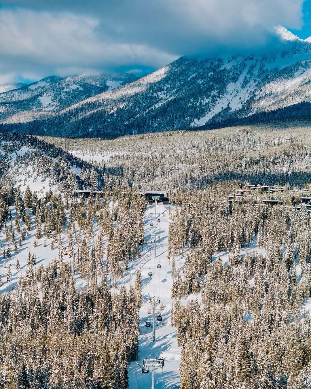 Un centro de esquí con telesilla, árboles cubiertos de nieve y montañas al fondo.