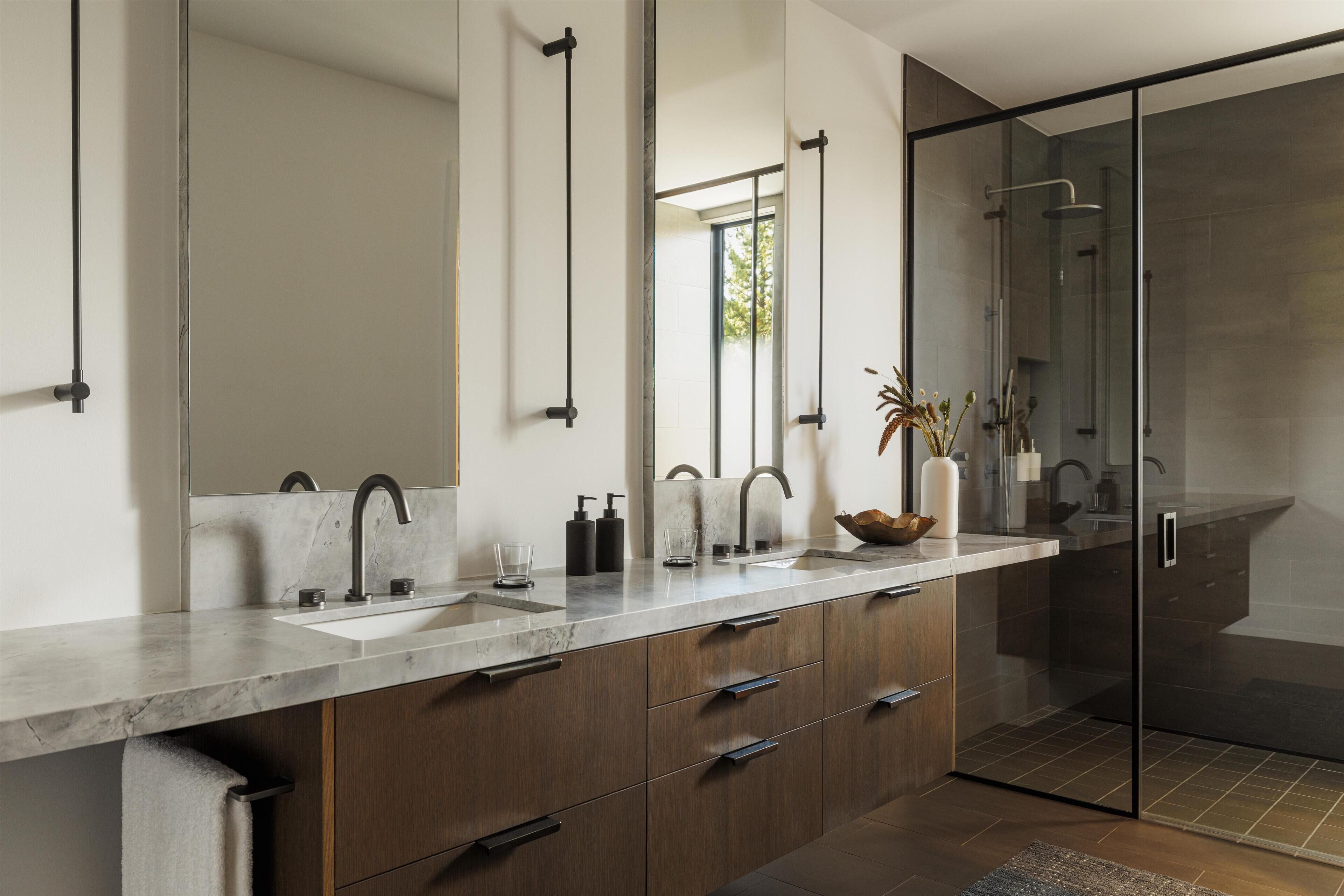 A modern bathroom with a large mirror, dual sinks, and a glass-enclosed shower.