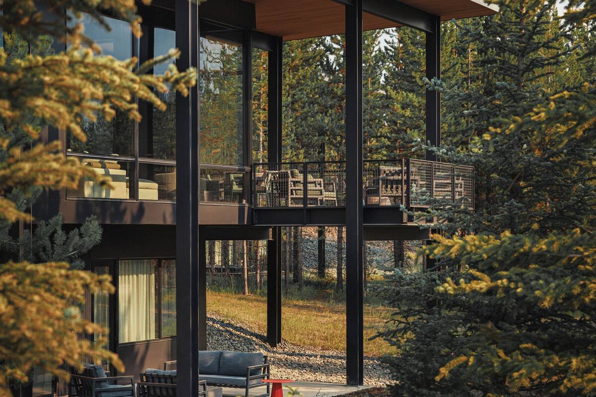 A modern house with a wooden deck, large windows, and a view of the surrounding forest.
