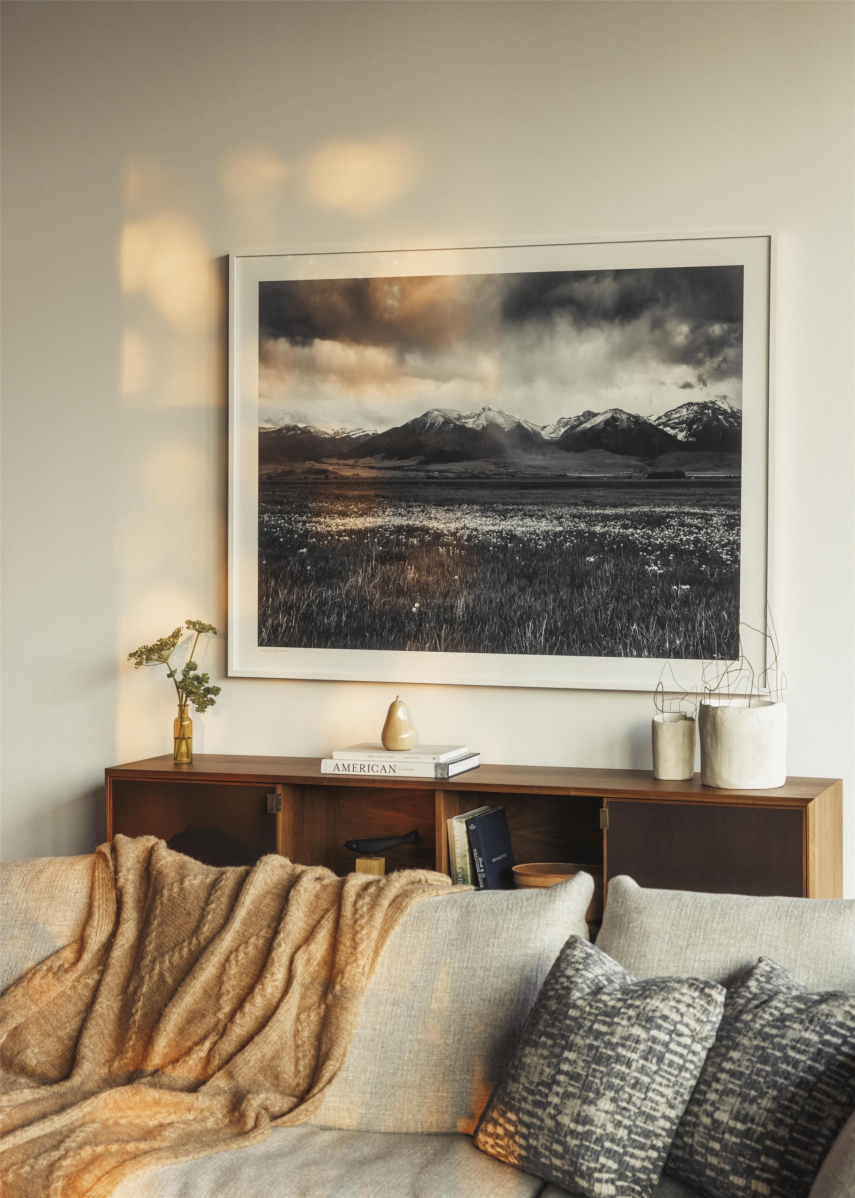 En stue med et stort, indrammet landskabsmaleri, et træbord og en sofa med puder.