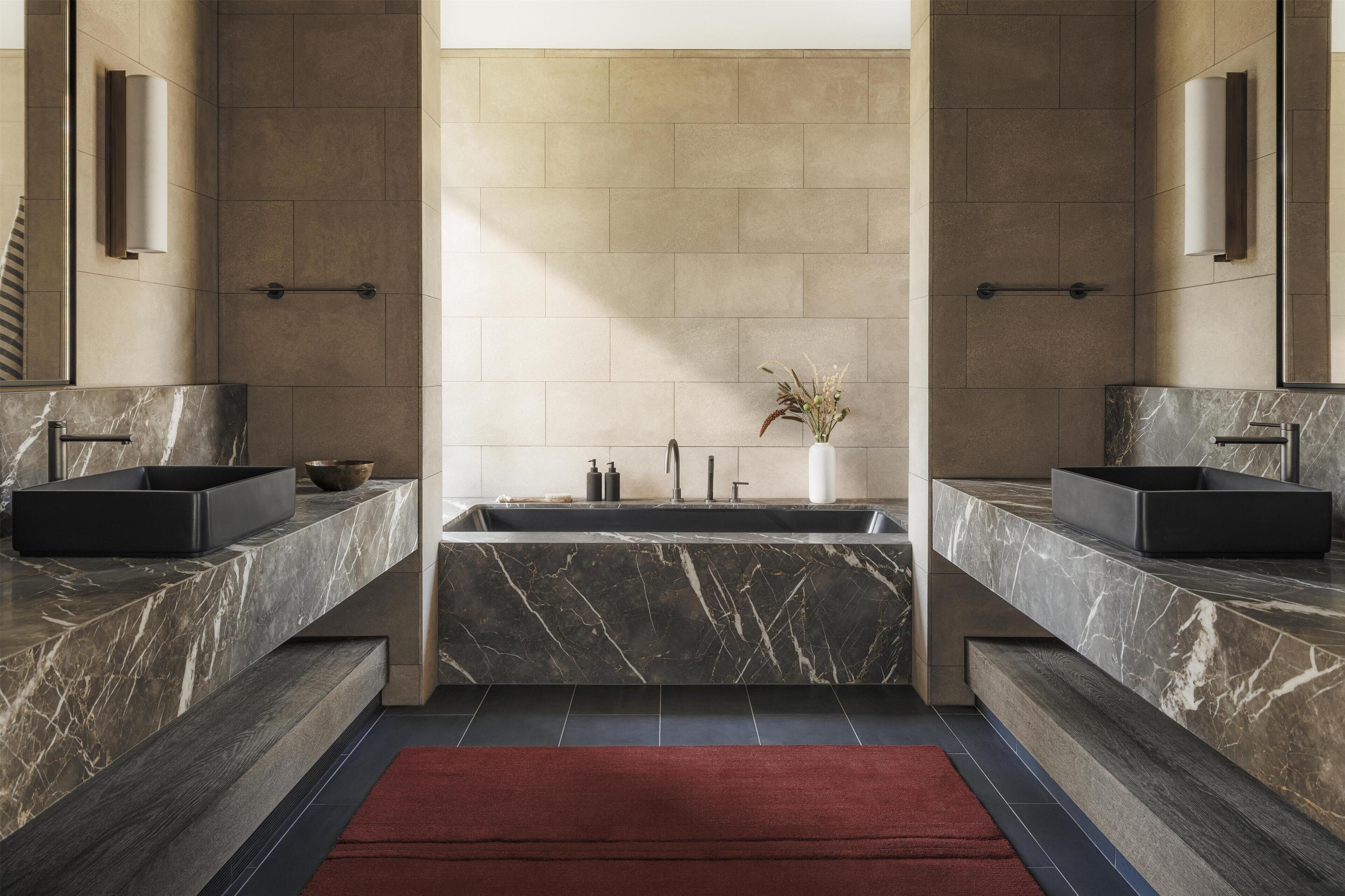 A modern bathroom with two sinks, a central bathtub, and a red rug.